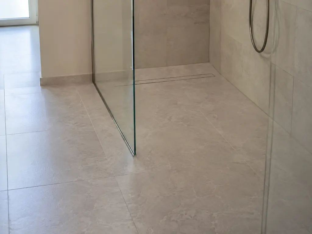 Kantenloser Übergang vom Fliesenboden in eine bodengleiche Dusche, im Hintergrund eine schmale Ablaufrinne entlang der Wand