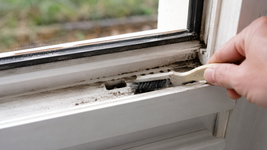 Falzraum am unteren Fensterrahmen wird mit einer Bürste gereinigt, die Entwässerungsöffnung ist sichtbar
