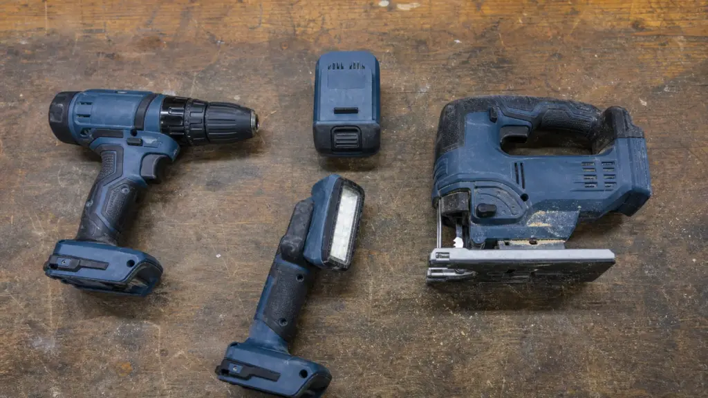 Akkuschrauber, Stichsäge und Handlampe liegen nebeneinander, dazwischen ein einzelner Wechselakku