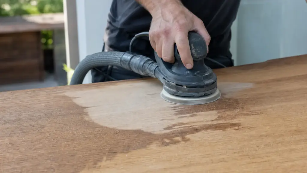 Exzenterschleifer entfernt einen dunklen Wasserfleck aus einer Massivholz-Arbeitsplatte, die geschliffene Stelle ist deutlich heller
