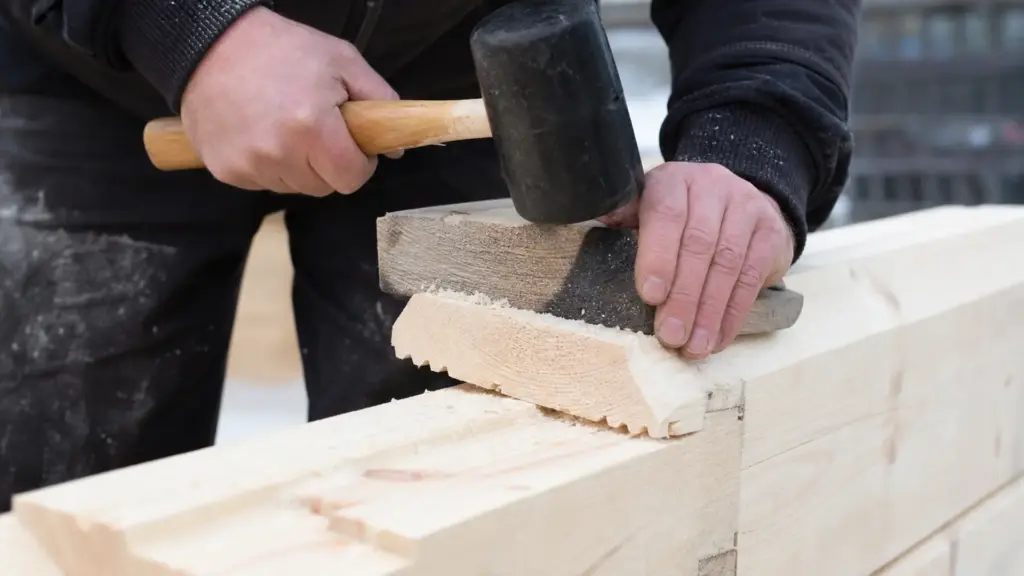 Gummihammer treibt über ein Schlagholz eine Blockbohle in die darunterliegende Nut