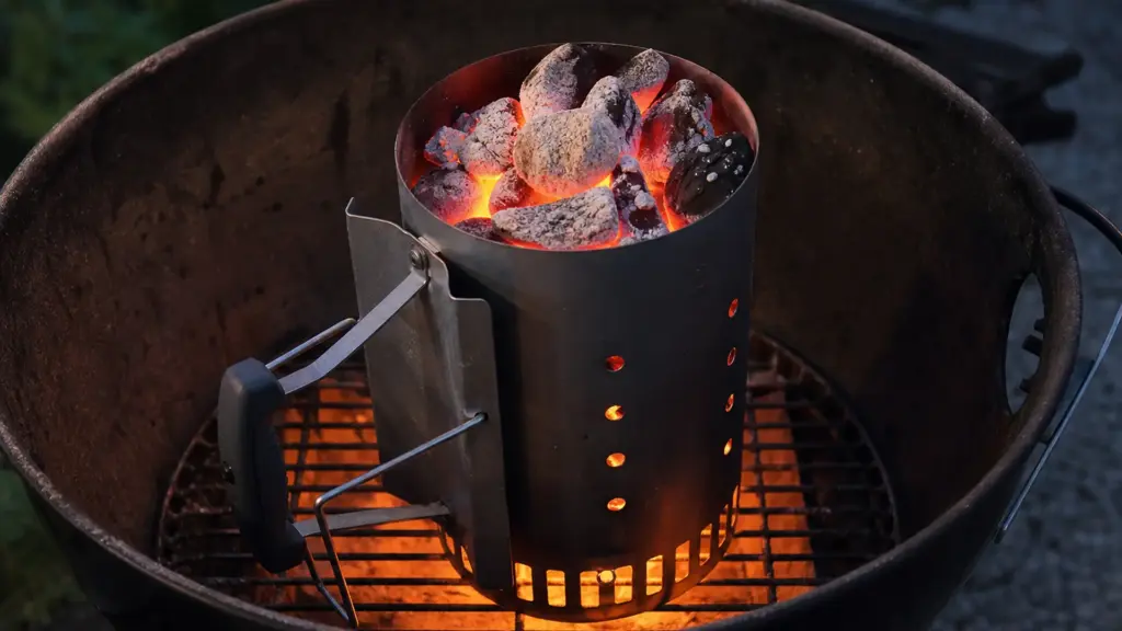 Anzündkamin mit durchglühender Holzkohle steht auf dem Kohlerost eines Kugelgrills