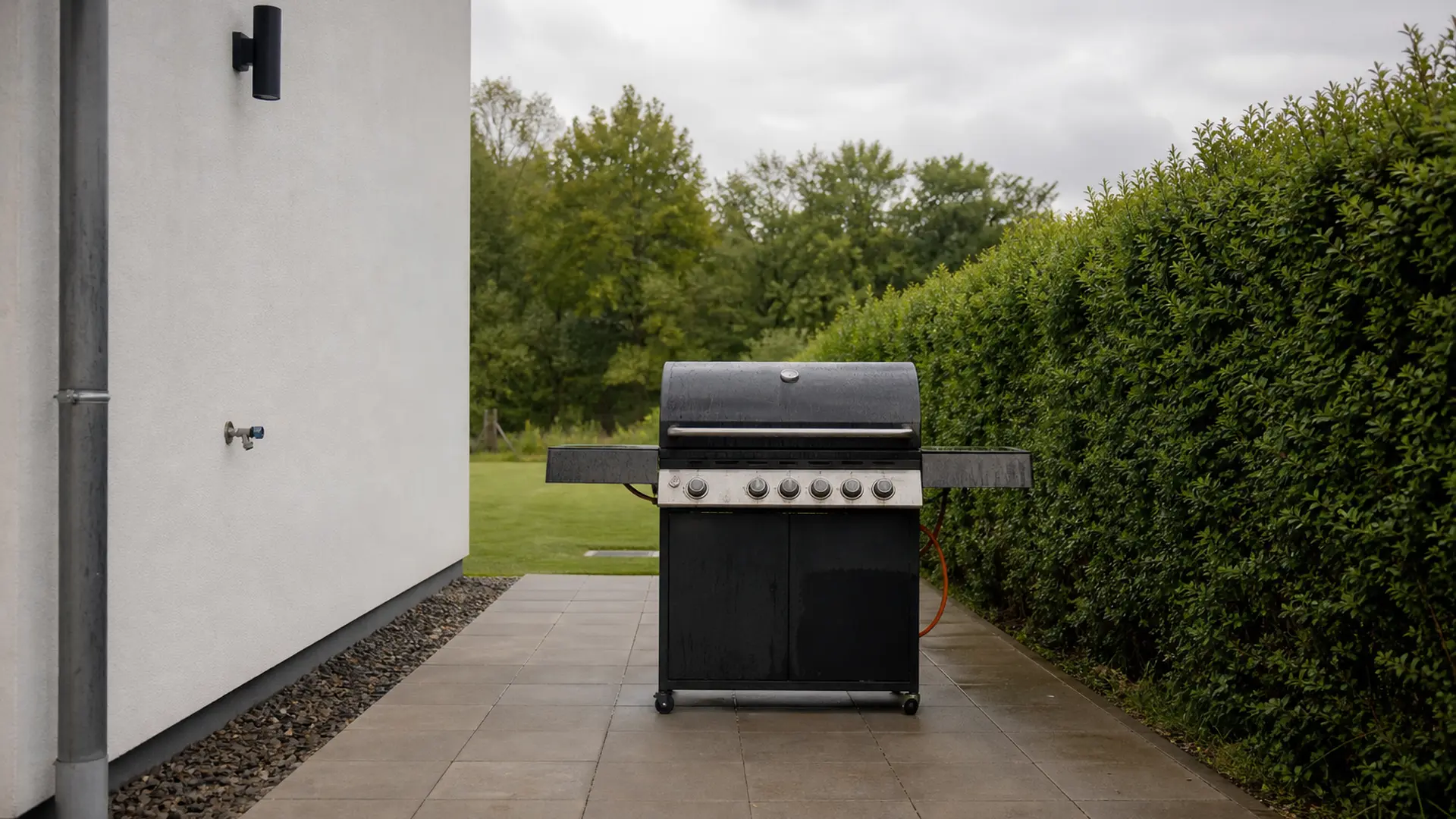 Grill steht mit deutlichem Abstand zur Hauswand und zur Hecke auf einer festen Plattenfläche