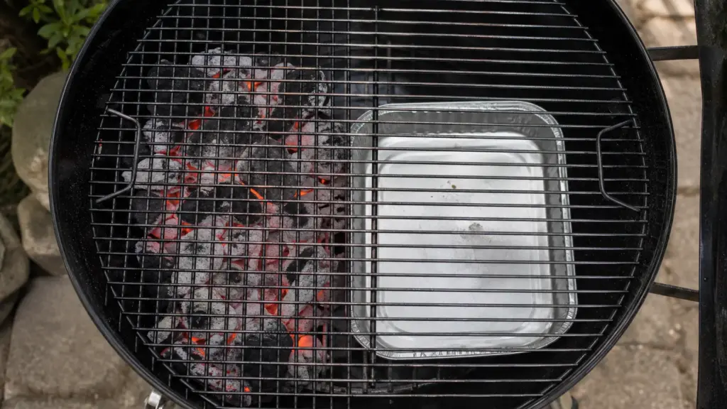 Kugelgrill mit Kohle nur auf einer Seite, auf der freien Seite steht eine Aluschale unter dem Rost