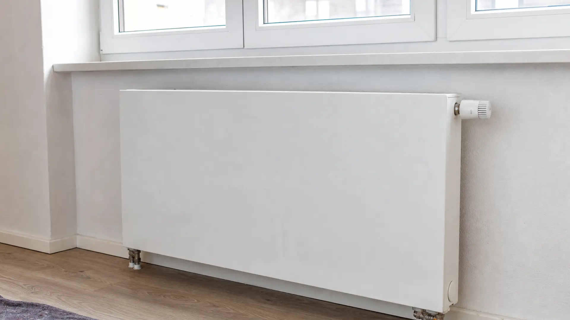 Flacher Kompaktheizkörper unter einem Fenster mit sichtbarem Anschluss und Thermostat