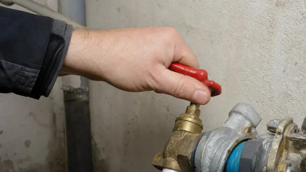 Hand schließt den Hauptabsperrhahn der Wasserleitung im Keller