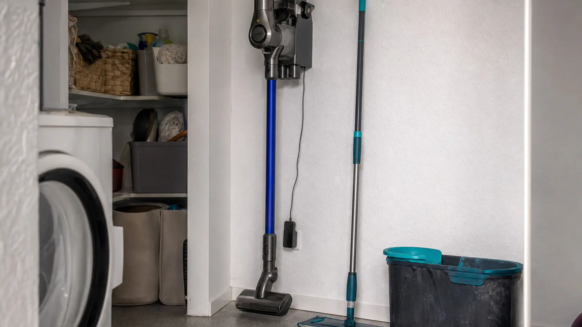 Akku-Stielstaubsauger in der Wandhalterung, daneben Eimer und Mopp