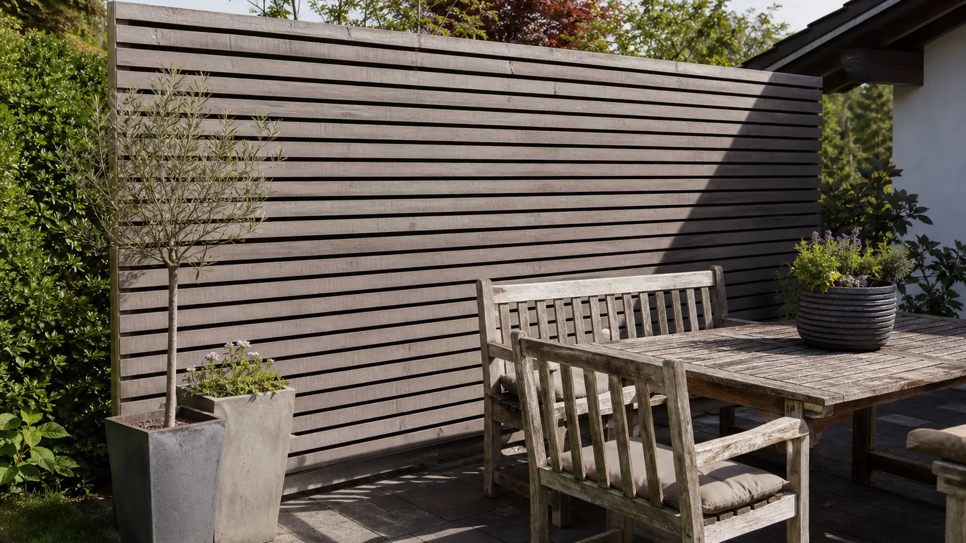 Sichtschutzwand aus waagerechten Holzlamellen grenzt einen Terrassenbereich mit Sitzgruppe ab