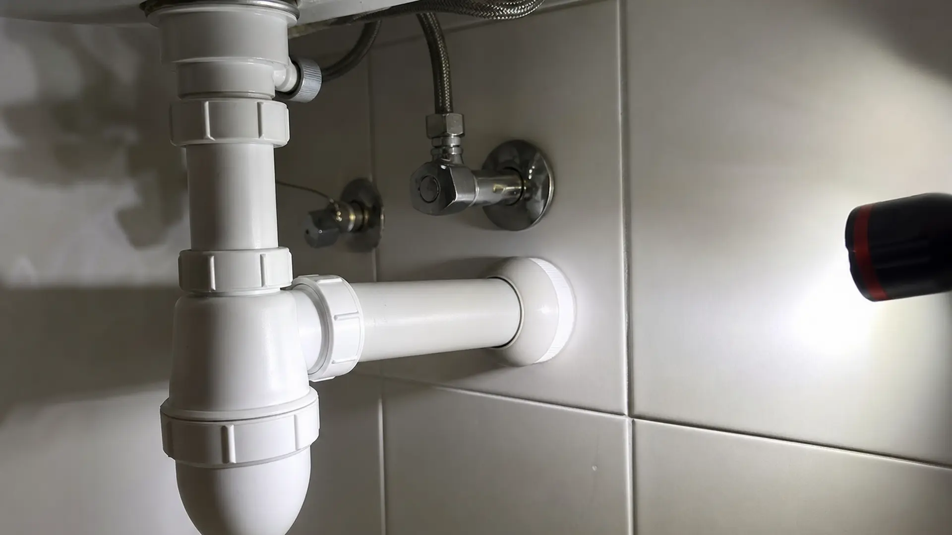 Weißer Kunststoff-Flaschensiphon unter einem Waschbecken, sauber ausgerichtet mit Anschluss zur Wandmuffe