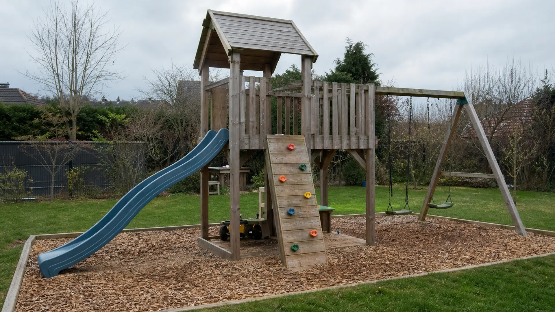 Spielturm mit Rutsche im Garten, darunter und ringsum eine Fläche mit Holzhackschnitzeln