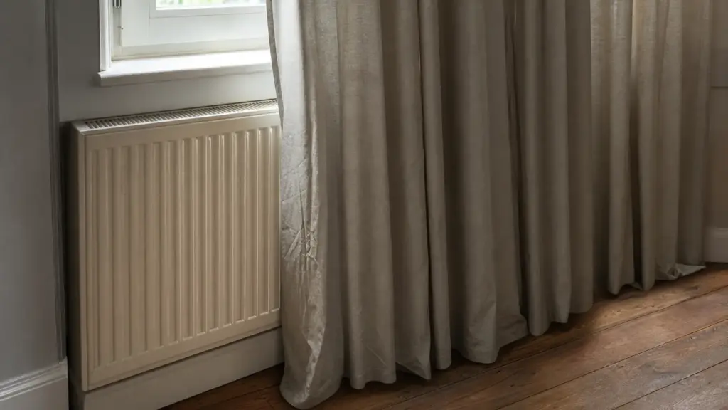 Heizkörper hinter einem langen Vorhang, der Thermostatkopf ist vom Stoff verdeckt