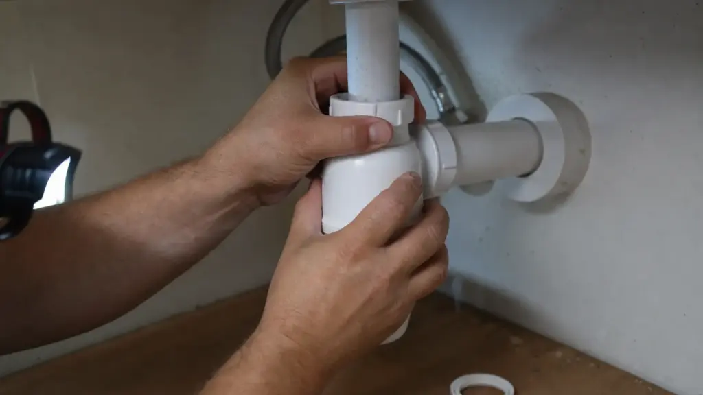 Hände ziehen die Überwurfmutter eines Flaschensiphons unter einem Waschbecken von Hand fest