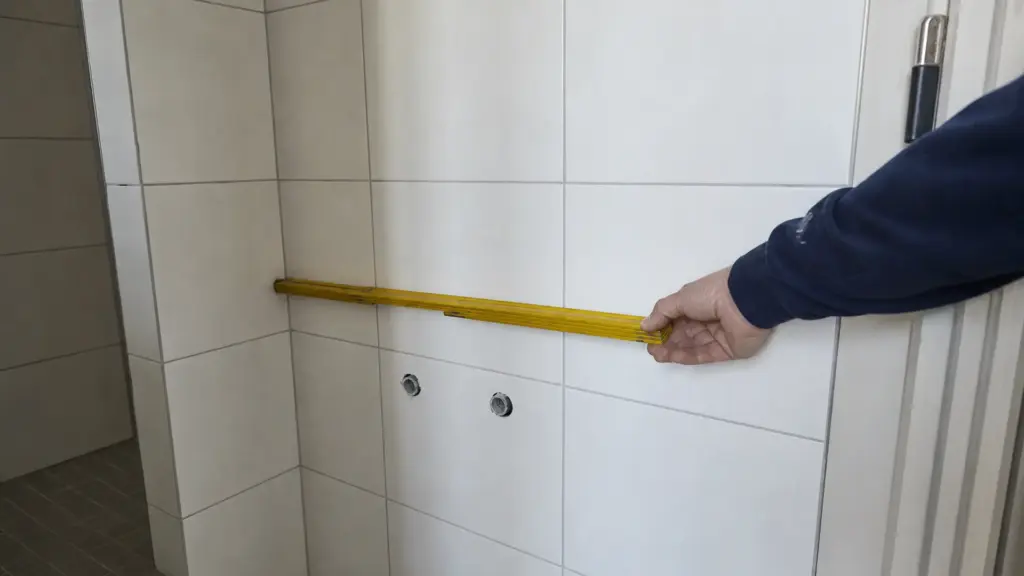 Hand hält einen Zollstock waagerecht an die Wand über einem freien Waschtischplatz und misst die verfügbare Breite