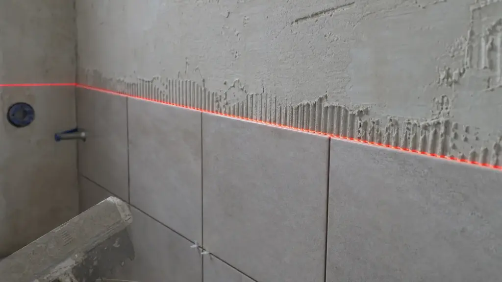 Waagerechte Laserlinie verläuft über eine halb gefliste Wand als Höhenreferenz