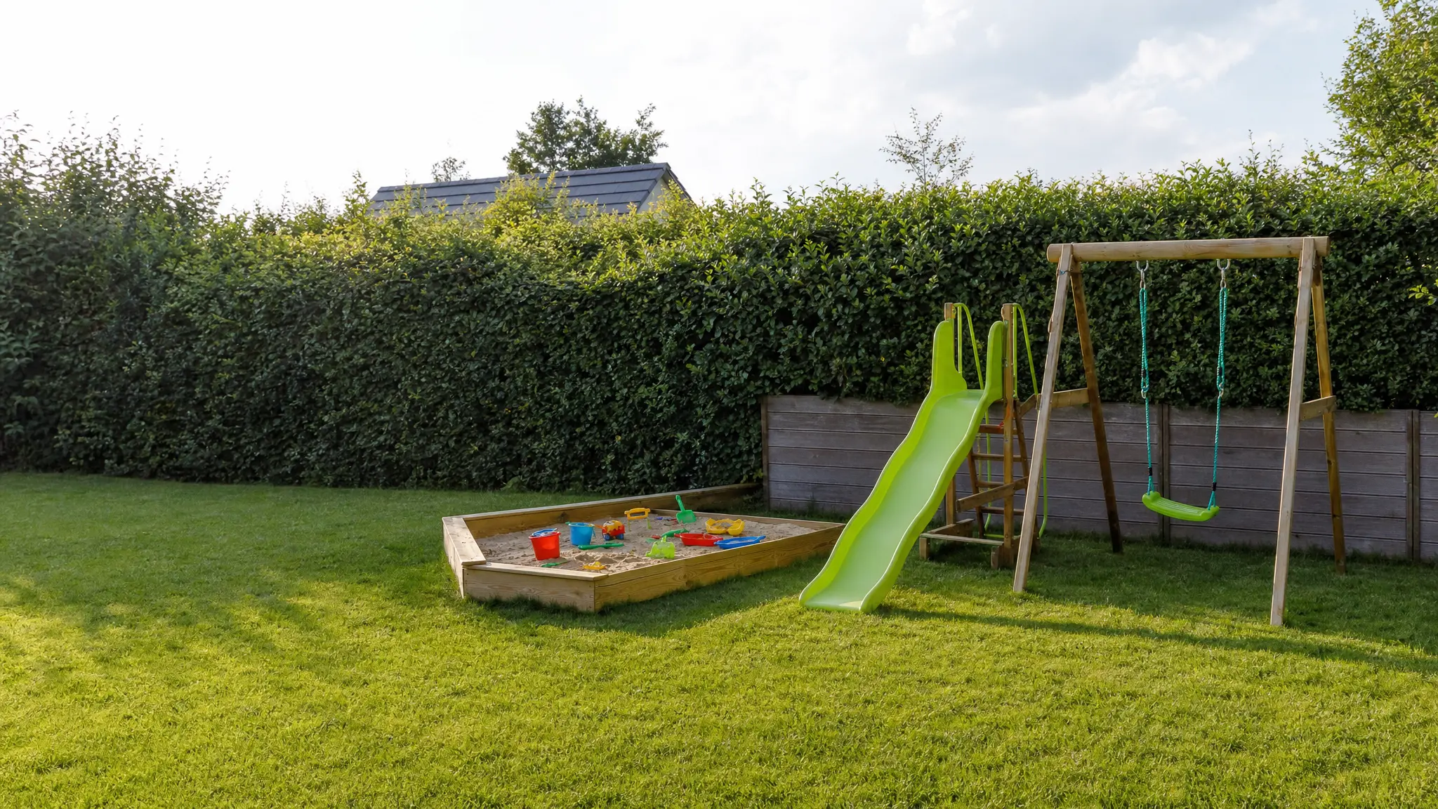 Ein Sandkasten, eine Rutsche und eine Schaukel stehen auf einer sonnigen Gartenwiese