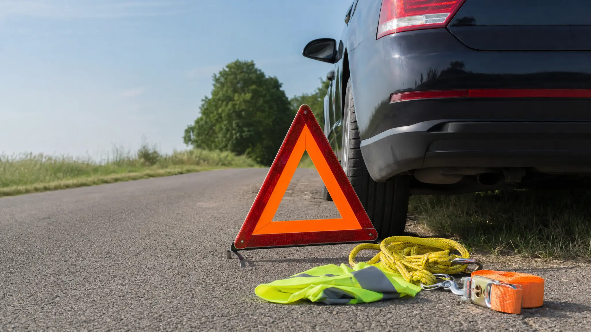 Ein Warndreieck, eine Warnweste und ein Abschleppseil liegen neben einem Auto am Straßenrand