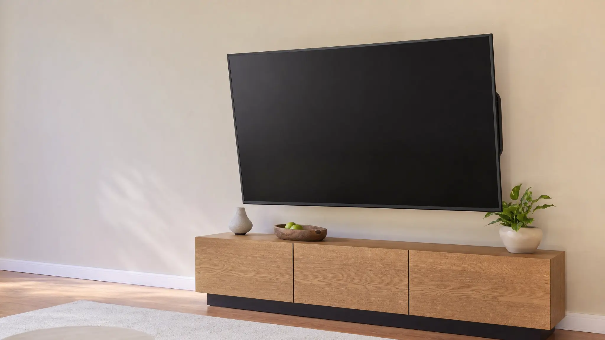 Ein ausgeschalteter Flachbildfernseher hängt an einer Wandhalterung über einem Sideboard im Wohnzimmer