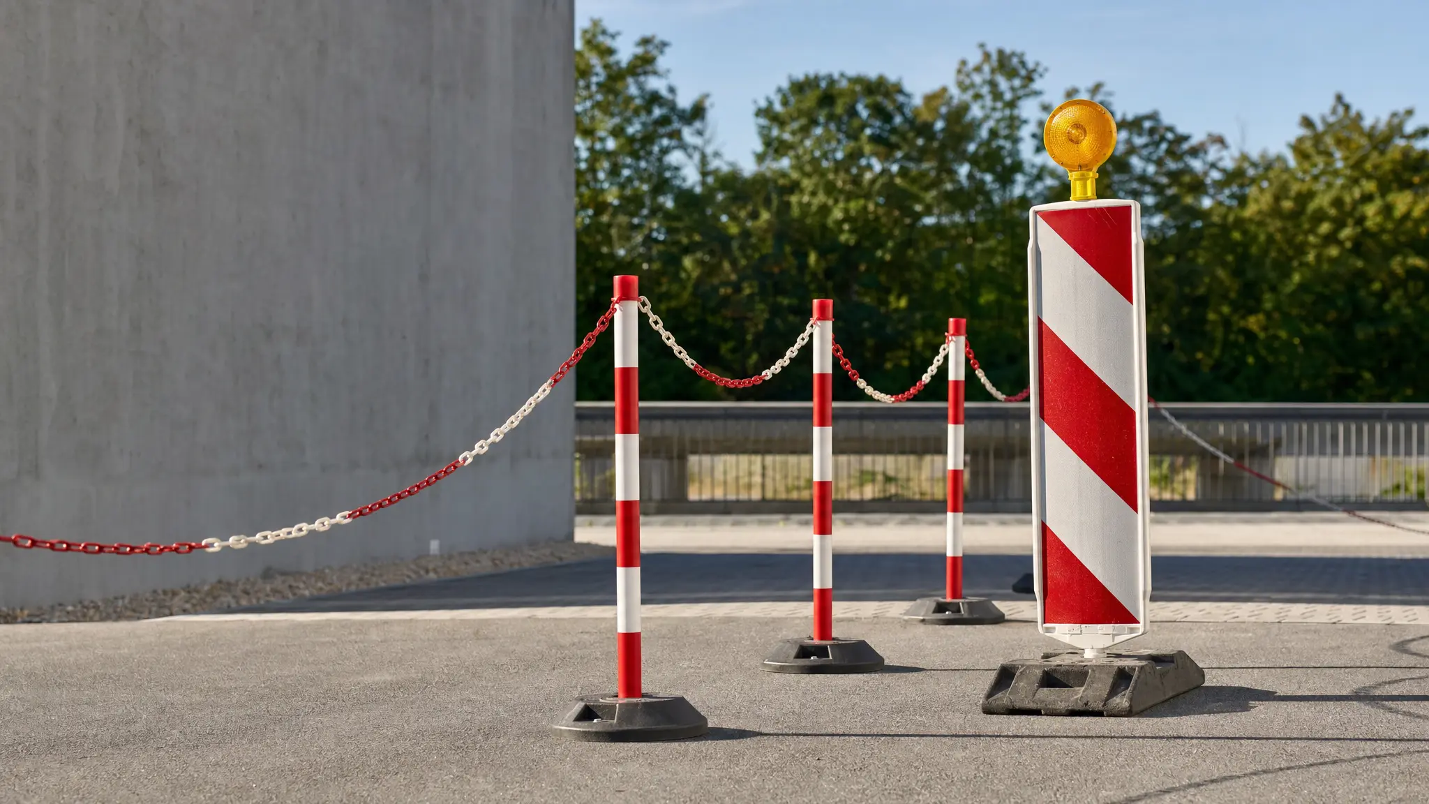 Rot-weiße Leitpfosten, Absperrpfosten mit Kette und eine Warnbake sichern eine Baustellenfläche auf Asphalt