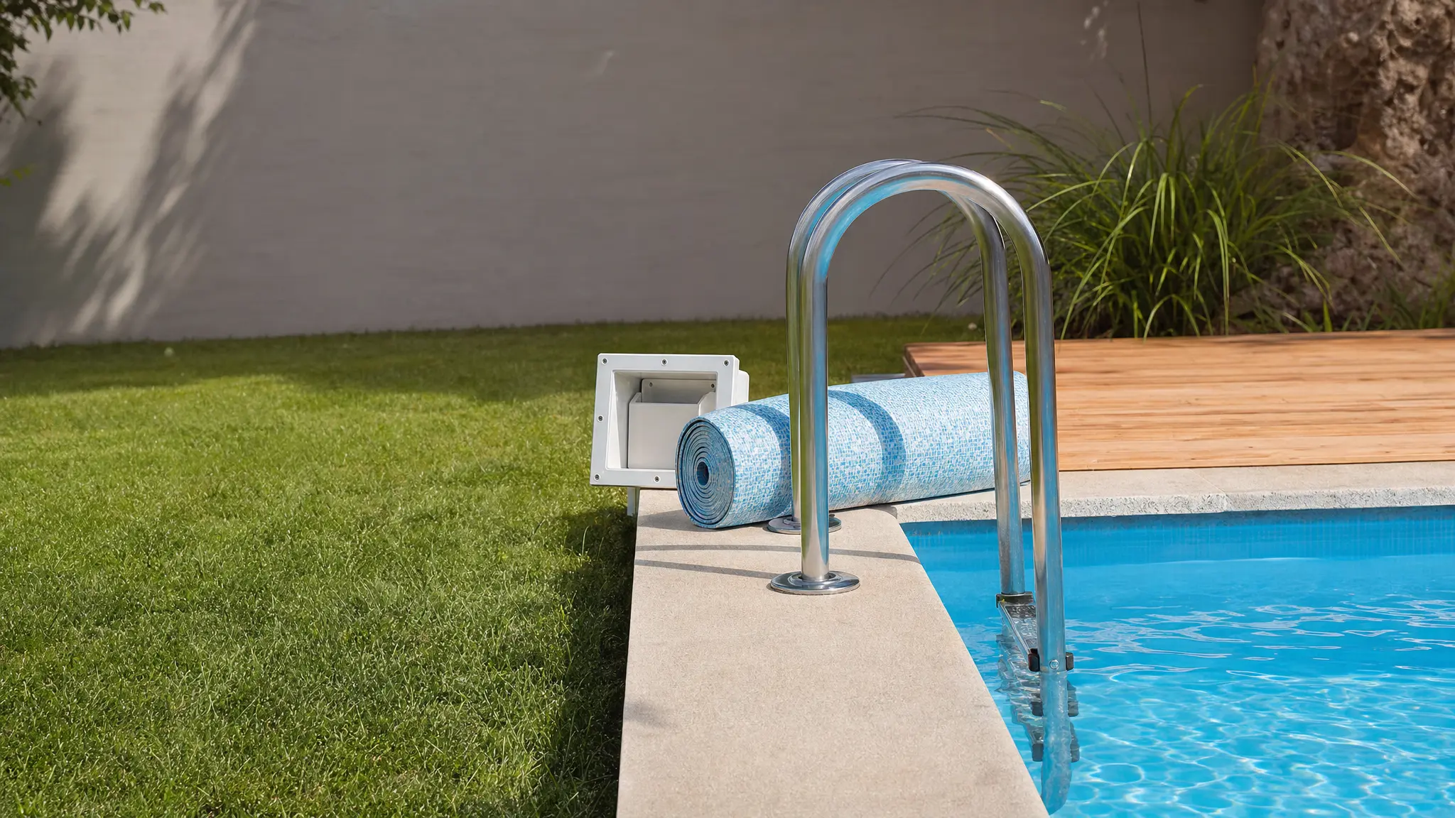 Eine Edelstahl-Poolleiter und aufgerollte Poolfolie liegen am Rand eines Gartenpools